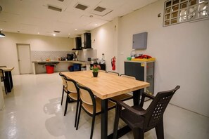 A dining area with a wooden table and chairs, a kitchen in the background, and a fire extinguisher mounted on the wall. - Kingston Hotel 6 @ Changkat Bukit Bintang (Kuala Lumpur)
