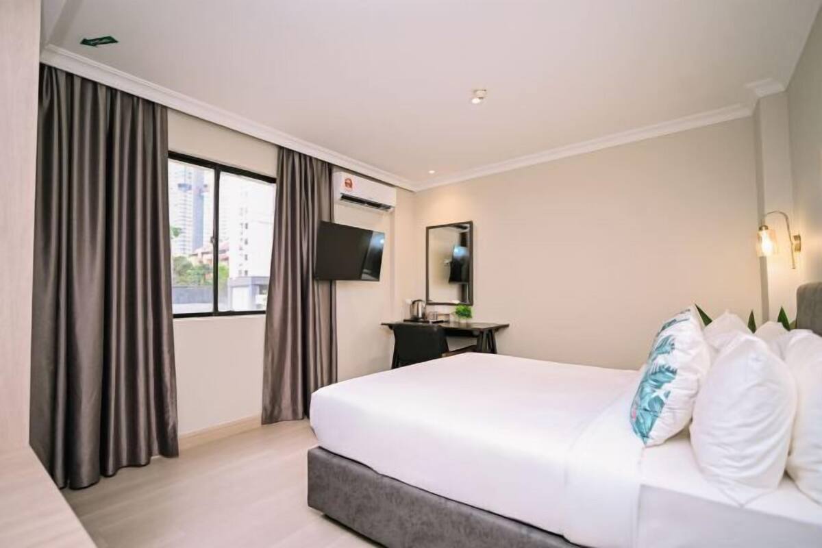 A hotel room with a bed, a desk, a chair, a TV, and a window with curtains.