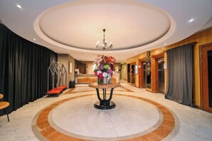 Un hall de hotel con mostrador de recepción, una araña de cristal y un diseño de piso circular.