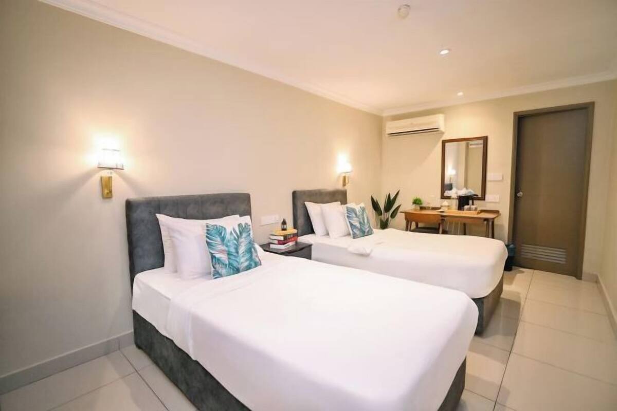 A hotel room with two beds, a desk, a chair, and a mirror.