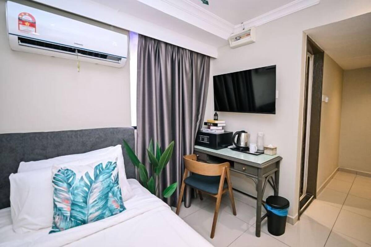 A hotel room with a bed, a desk, a chair, a TV, and an air conditioning unit.