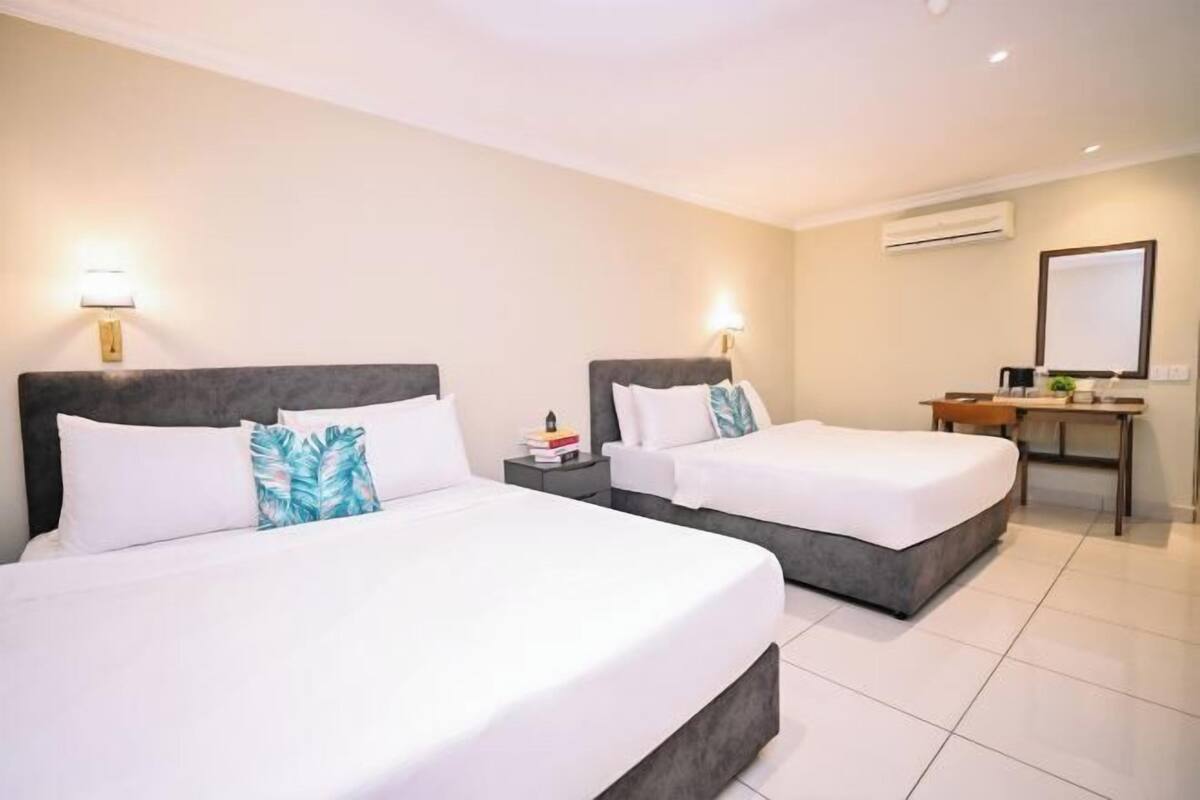 A hotel room with two beds, bedside tables, a desk, and an air conditioning unit.
