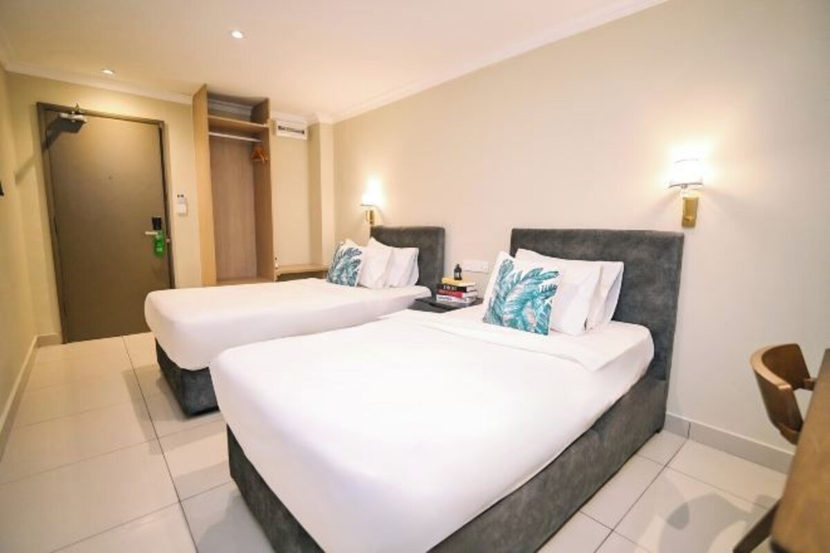 A hotel room with two beds, a wardrobe, a bedside table with a lamp, and a chair.