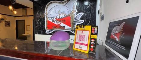 Un mostrador de recepción con un letrero con temática de tiburón, un código QR y una ilustración enmarcada de un tiburón.