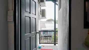 A doorway leading to a balcony with a red mat, a black railing, and a building with a grey roof in the background.