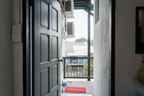 A doorway leading to a balcony with a red mat, a black railing, and a building with a grey roof in the background. - Project X Scuba (Semporna)