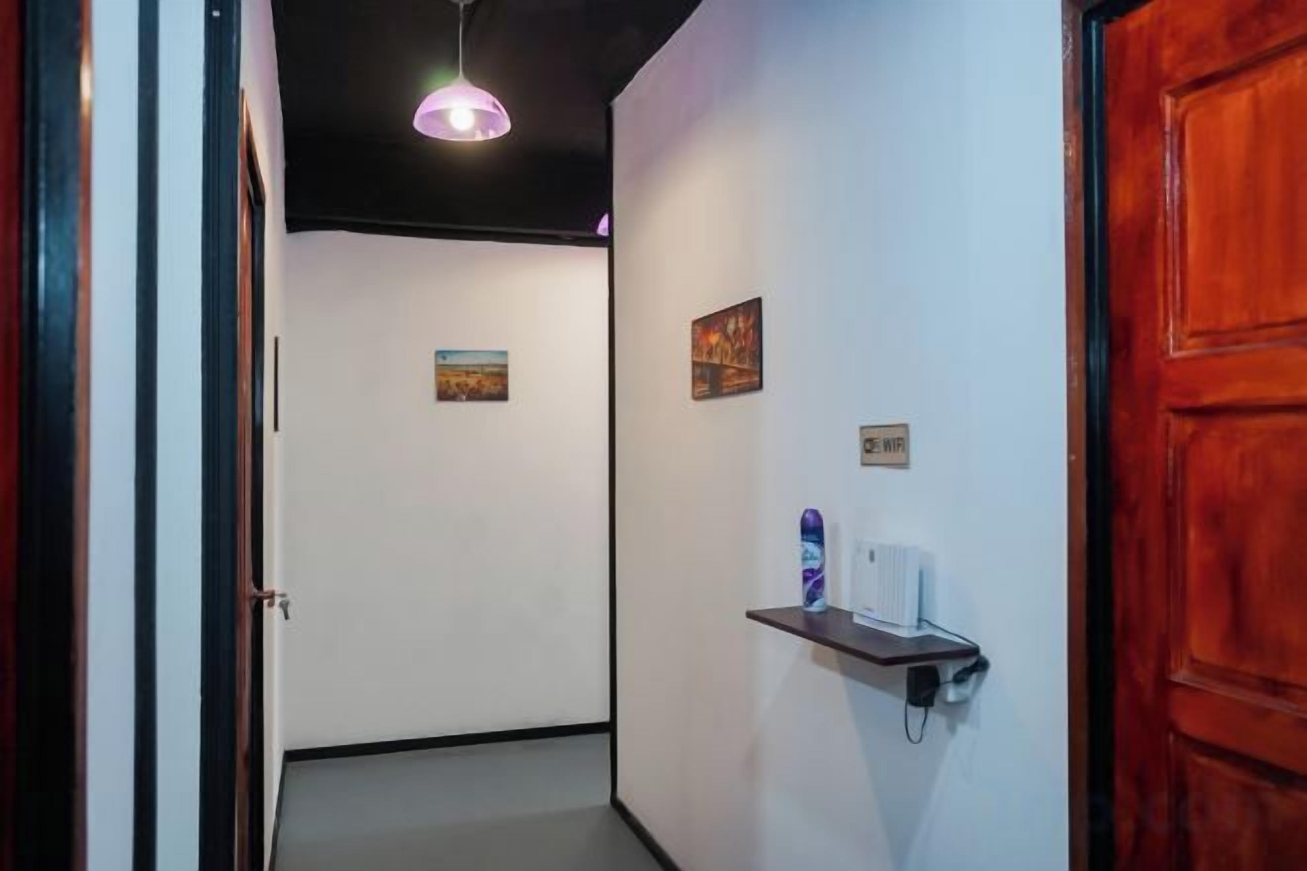 Un pasillo con puerta de madera, un estante con objetos y un aplique.