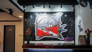 A reception desk with a shark-themed logo and a marble wall. - Project X Scuba (Semporna)