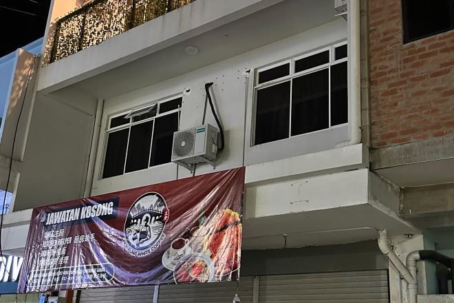 Un edificio con un gran cartel publicitario de un restaurante. Hay dos ventanas en el piso superior y una unidad de aire acondicionado montada en la pared.