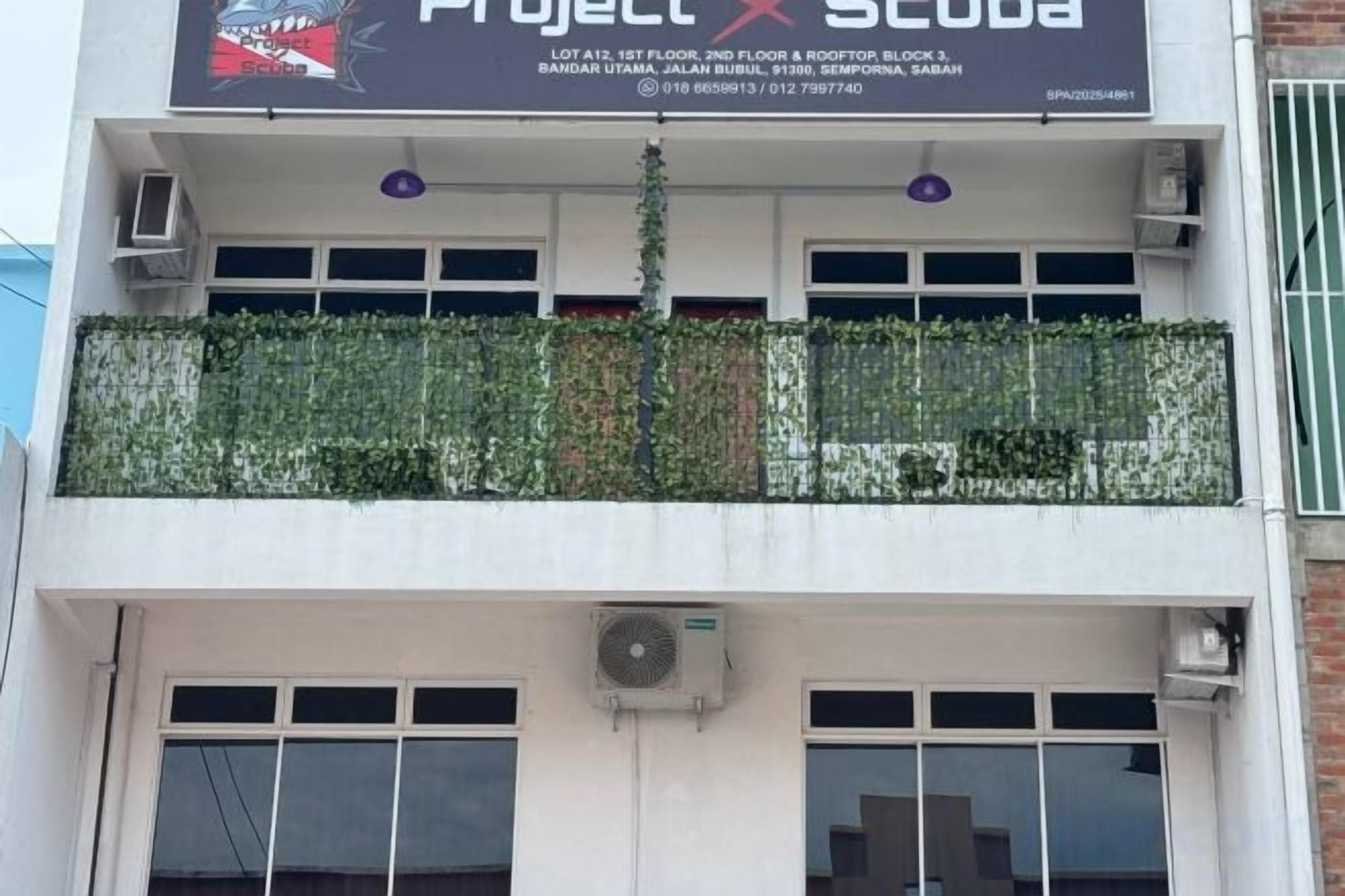 Un edificio con un letrero que dice 'Project X Scuba' y un balcón con plantas.