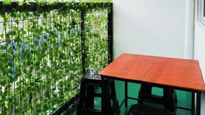 A small balcony with a green leafy partition, a wooden table, and two black stools. - Project X Scuba (Semporna)