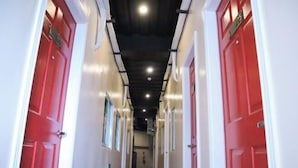 A corridor with red doors and white walls, leading to a room with a bed and a window. - CITISTYLE INN (Davao)