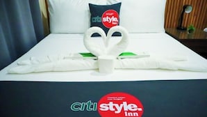 A hotel bed with a heart-shaped towel arrangement, a pillow with 'citi style inn' branding, and a logo on the bedspread. - CITISTYLE INN (Davao)