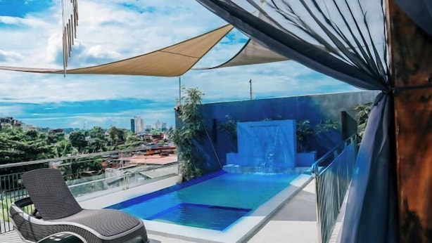 A modern outdoor pool area with a lounge chair, a waterfall feature, and a city view. - CITISTYLE INN (Davao)