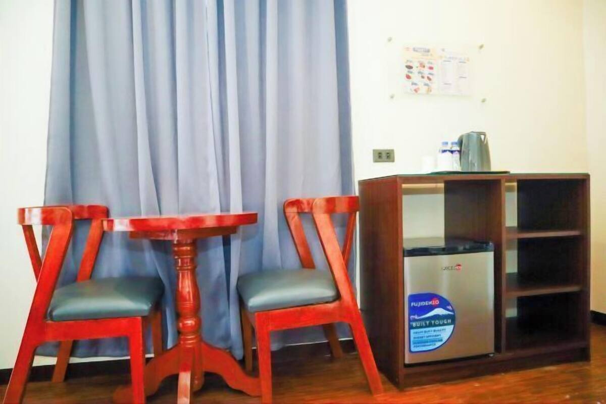 A room with a wooden table and two chairs, a cabinet with a Fujifilm label, and a blue curtain.