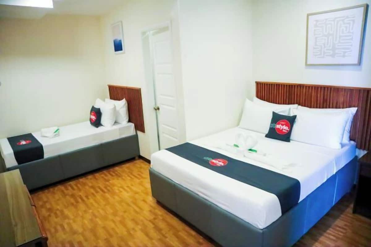 A hotel room with two beds, a wooden floor, and a white door.