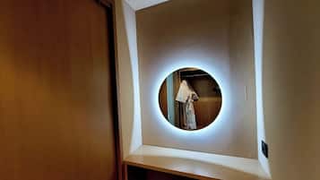 Un espejo pequeño y redondo con luz alrededor, fijado a la pared en un rincón de la habitación.