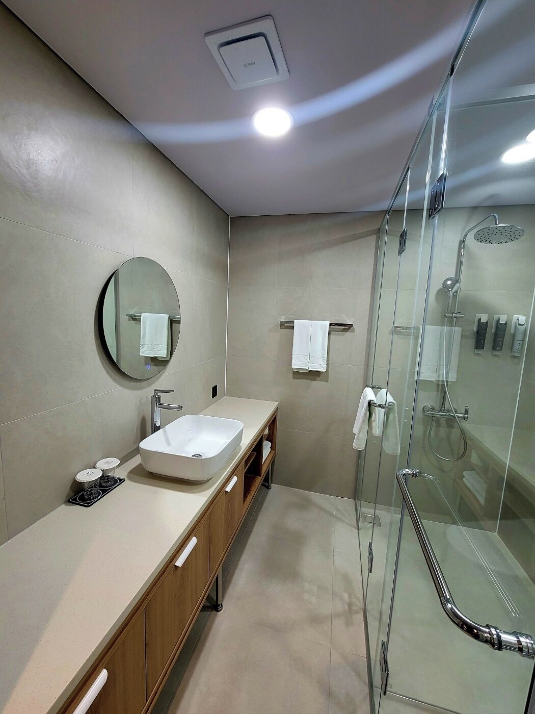 A modern bathroom with a glass-enclosed shower, a round mirror, a sink, and a vanity with a cabinet.