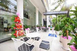 An outdoor seating area with white chairs and tables, surrounded by potted plants and a decorative floral arrangement. - The Shilla Luxury I Hotel-더신라럭셔리호텔 (Ho Chi Minh City)