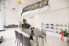 A hotel lobby with a reception desk, a dining area with a table and chairs, and a staircase with decorative railings. - The Shilla Luxury I Hotel-더신라럭셔리호텔 (Ho Chi Minh City)