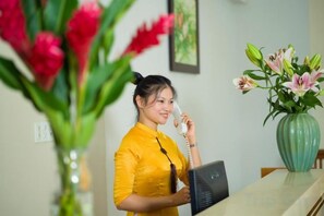 Zona de recepción con recepcionista, un mostrador y un florero con flores.