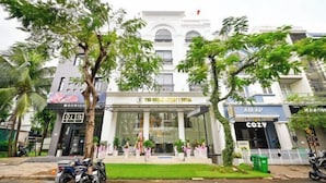Un hôtel avec une entrée principale, entouré de palmiers et bordé de motos garées.