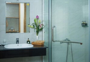 Un baño con un lavabo blanco, un espejo, un jarrón con flores y una cabina de ducha de vidrio.