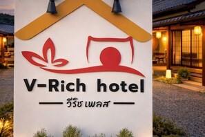 Et hotelskilt med en stiliseret logo og navnet 'V-Rich hotel' på engelsk samt et andet skriftsystem.