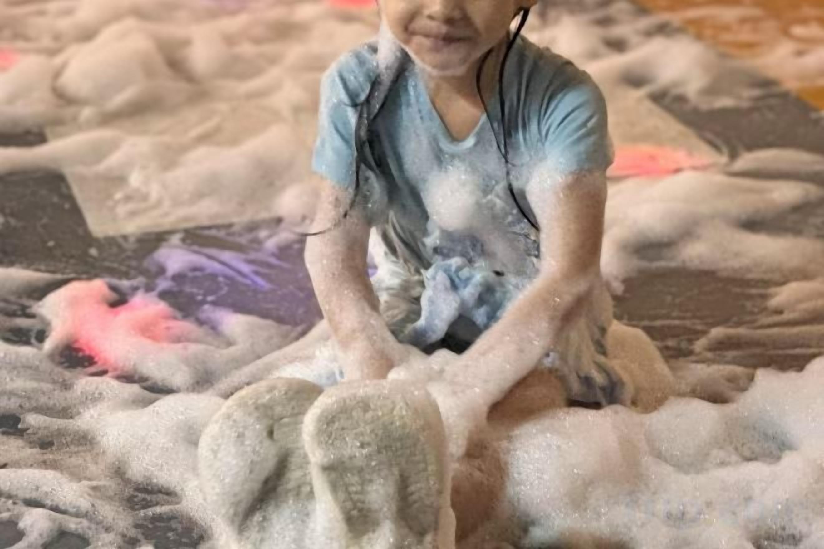 A child sitting on a textured surface with foam or sand.
