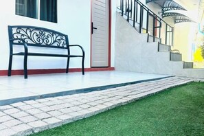 A bench outside a building with a staircase and a door. - V RICH (Roi Et)