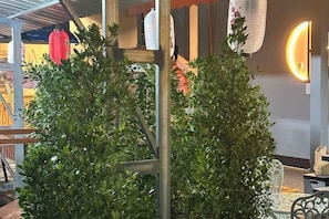 Una habitación con estructura de techo de madera, una planta en maceta y una lámpara fijada a la pared.