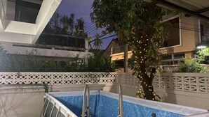 A swimming pool with a ladder, surrounded by a white fence and a tree with lights. - Luck viia 2 (Bangkok)