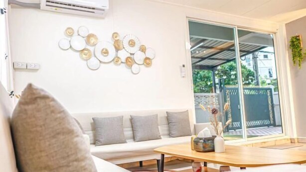 A modern living room with a white sofa, a wooden coffee table, and a decorative wall piece. - Luck viia 2 (Bangkok)