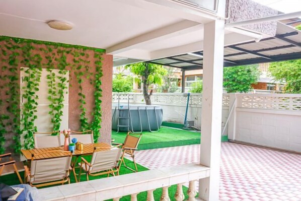 An outdoor patio with a table and chairs, a covered seating area, and a view of a fenced yard. - Luck viia 2 (Bangkok)