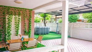 A covered patio area with a table and chairs, a small garden with artificial grass, and a pool. - Luck viia 2 (Bangkok)