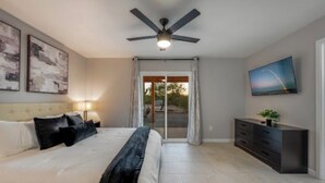 A modern bedroom with a bed, a ceiling fan, a TV, and a sliding glass door to the outside.