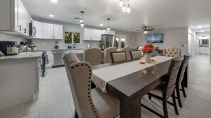 A spacious kitchen with white cabinets, a dining area with a wooden table and chairs, and a ceiling fan.