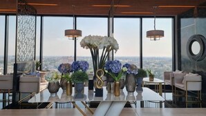Un coin repas avec une table dressée pour quatre personnes, de grandes fenêtres et une vue sur la ville.