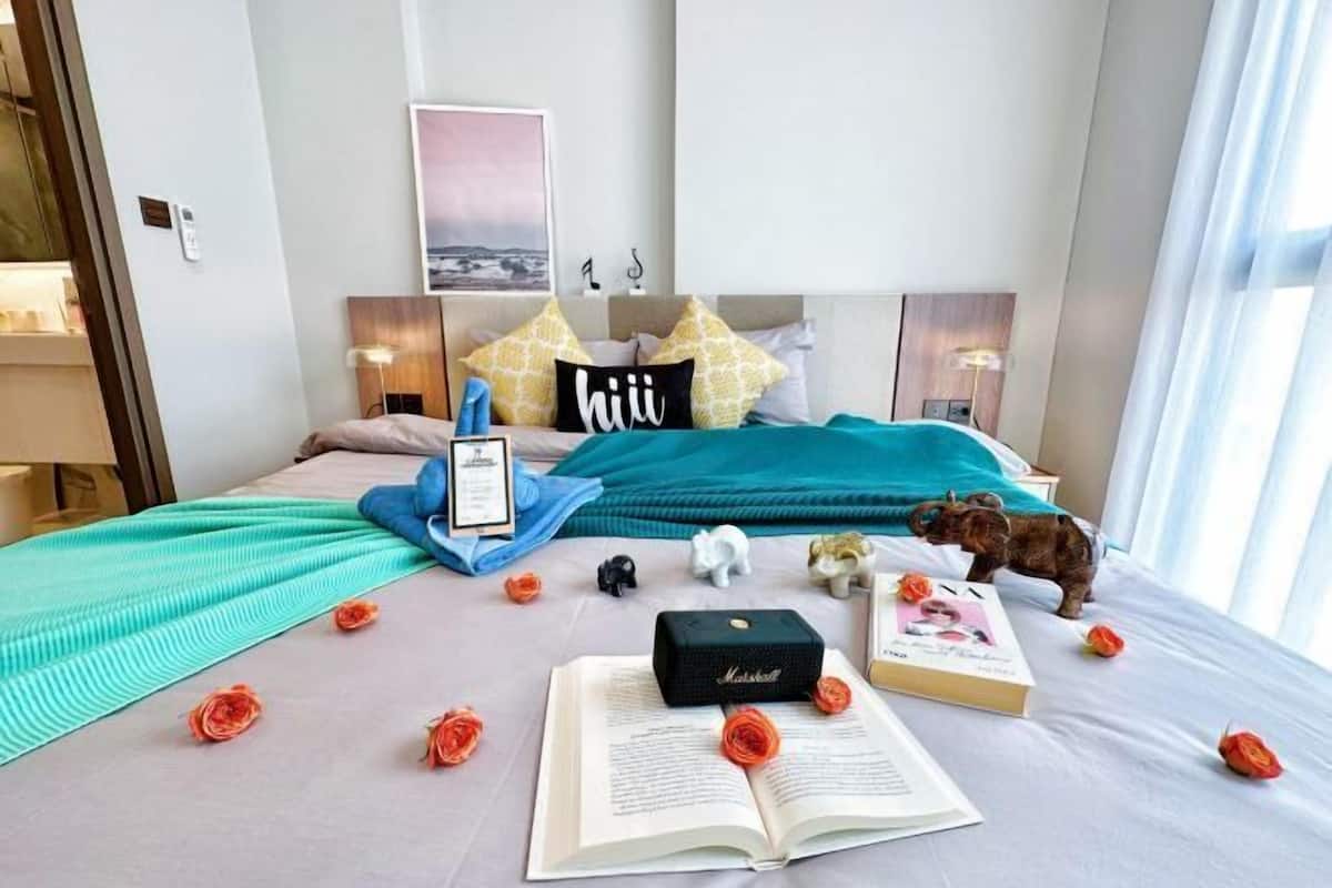 A neatly arranged hotel room with a bed, pillows, a framed picture, a small desk, and a window with curtains.