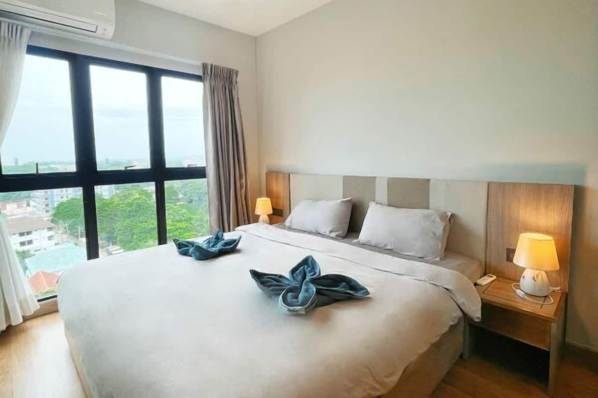 A hotel room with a large bed, two bedside lamps, and a view of a cityscape through a large window.