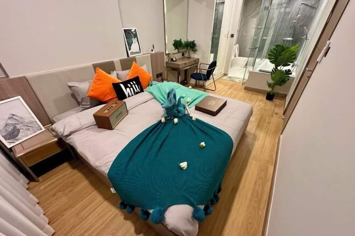 A modern bedroom with a bed, a desk, a chair, and a shower area.