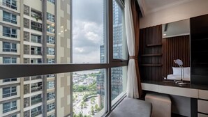 A modern hotel room with a large window, a desk, a chair, and a view of the cityscape.