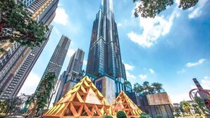 A modern urban area with high-rise buildings, including a prominent skyscraper. There are geometric structures in the foreground, possibly part of a public art installation or architectural feature.