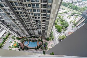 A high-rise building with a swimming pool surrounded by greenery.
