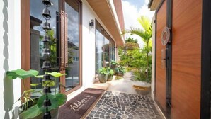 A modern hotel entrance with a stone-tiled pathway, potted plants, and a wooden door. - Alden Design Pool Villa (Pattaya)