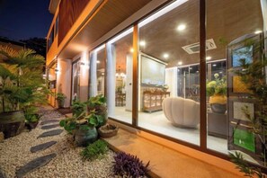 Un bâtiment moderne doté de grandes fenêtres en verre, d’un intérieur bien éclairé et d’un espace jardin agrémenté de plantes en pot.
