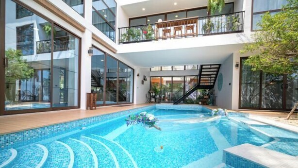 A modern house with a large indoor swimming pool, a balcony with outdoor seating, and a staircase leading to the upper floor. - Alden Design Pool Villa (Pattaya)