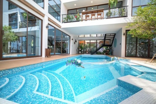 A swimming pool with a clear blue water design, surrounded by a wooden deck and glass walls. - Alden Design Pool Villa (Pattaya)