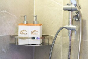 A bathroom with a shower, a glass shelf holding two bottles of shower gel, and a handheld showerhead. - Alden Design Pool Villa (Pattaya)