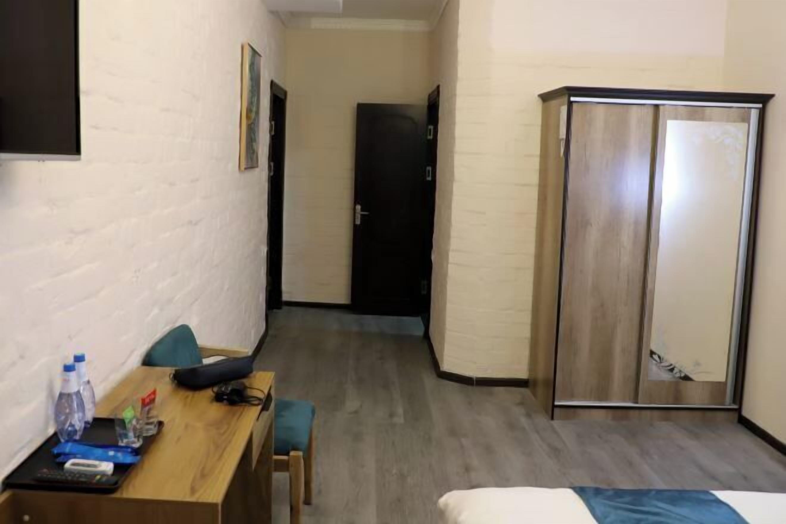 Een hotelkamer met een houten bureau, een bed, een kledingkast en een deur op de achtergrond.